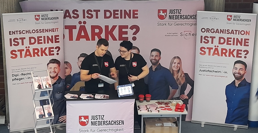 Stand der niedersächsischen Justiz bei der Berufsmesse TschüssSchule in Goslar mit Kollegen vor einem Tisch mit Werbematerialien